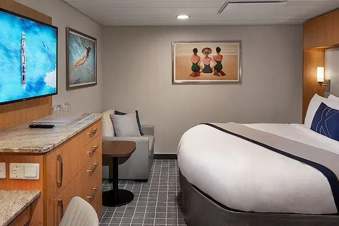 An Interior stateroom aboard Celebrity Xcel, king bed, sofa and desk with wood cabinetry