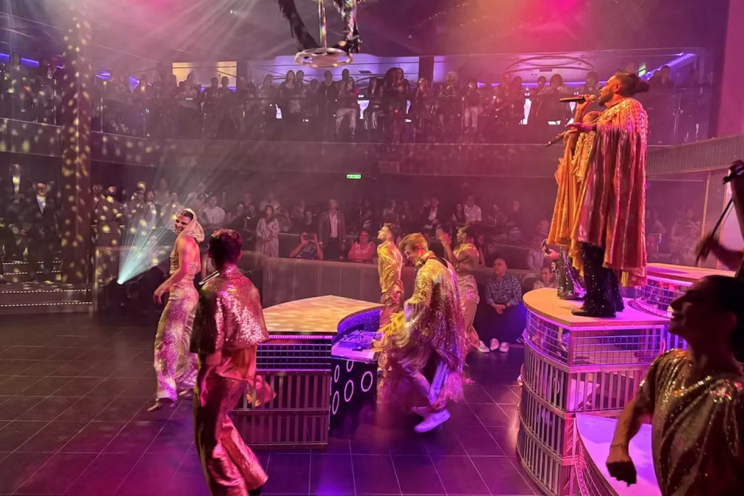 Two performers seated beneath a hanging canopy of roses in Chapters, with a flowered landscape on the LED wall behind
