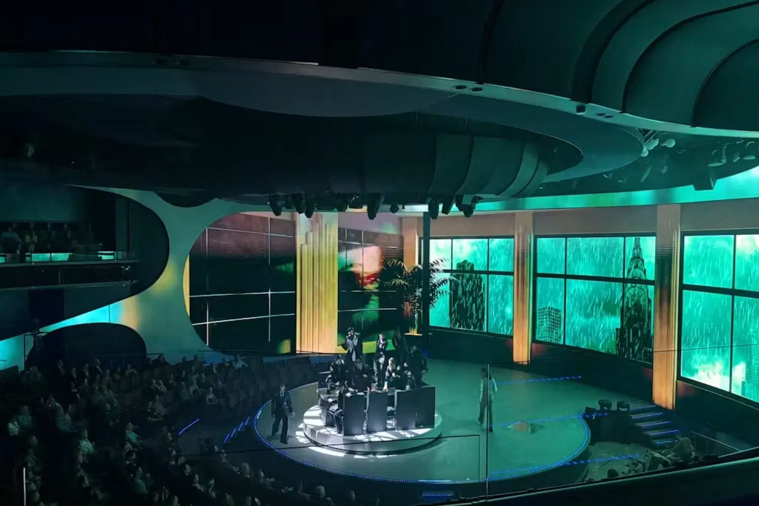 A full company number in The Theatre aboard Celebrity Xcel, dancers on the round stage before a lit street set